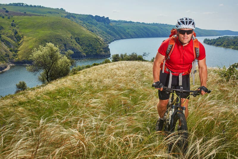 Cyklista przygodę na jego rowerze górskim przez zielonej łąki przeciw pięknemu niebu obraz stock Cyklista przygodę na jego rowerze górskim przez zielonej łąki przeciw pięknemu niebu obraz stock