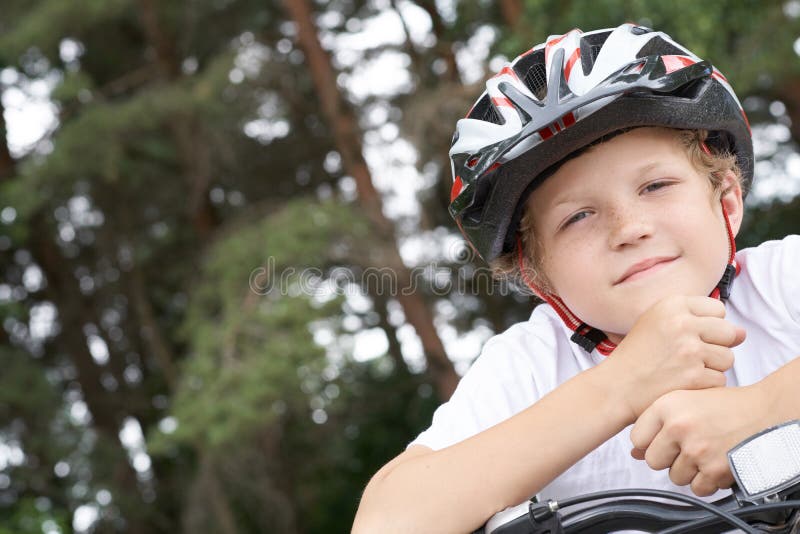 Cyklisten för den lilla kaukasiska pojken i skyddshjälmen satte huvudet på handledet på den cykel som ställer upp för kameran en arkivfoton