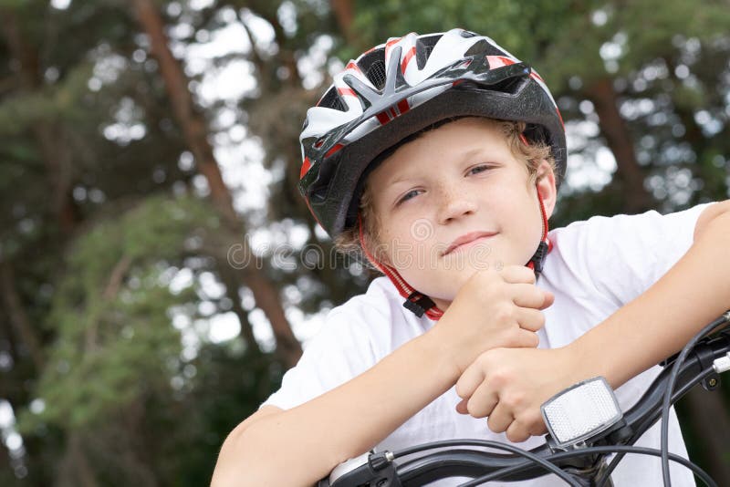 Cyklisten för den lilla kaukasiska pojken i skyddshjälmen satte huvudet på handledet på den cykel som ställer upp för kameran en royaltyfri fotografi