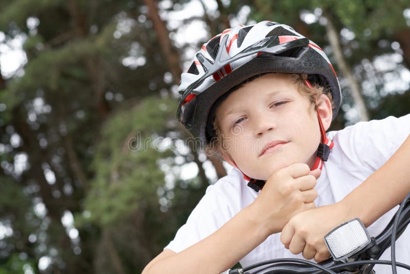 Cyklisten för den lilla kaukasiska pojken i skyddshjälmen satte huvudet på handledet på den cykel som ställer upp för kameran en arkivbilder