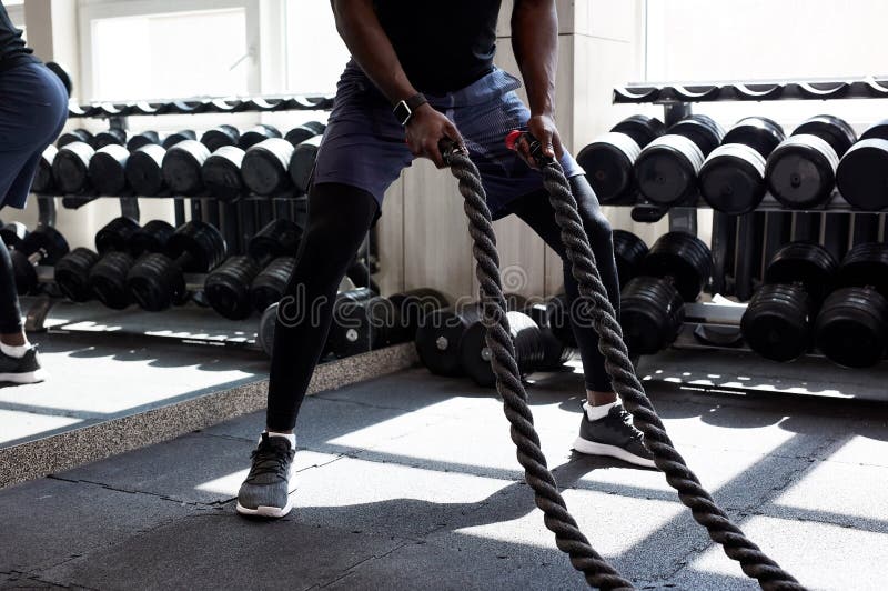 Czarni sportowcy uprawiający ćwiczenia na linach bojowych na siłowni krzyżowej