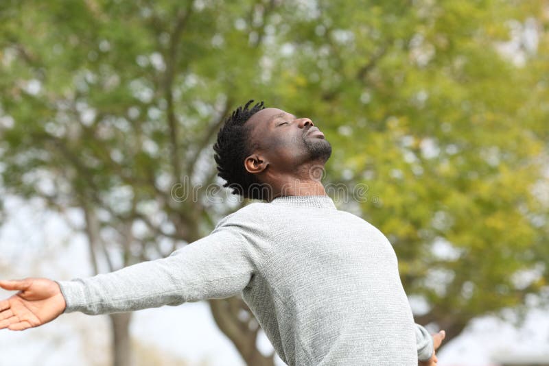 Czarny człowiek oddychający świeżym powietrzem wyciągającym ramiona w parku