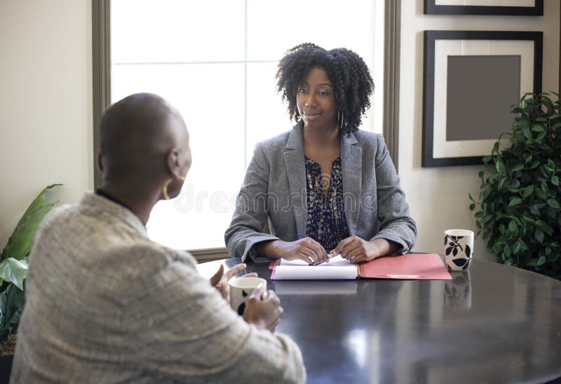 Black African American female businesswomen talking in an office.  The two women looks like a start up co workers or small business partners. Black African American female businesswomen talking in an office.  The two women looks like a start up co workers or small business partners