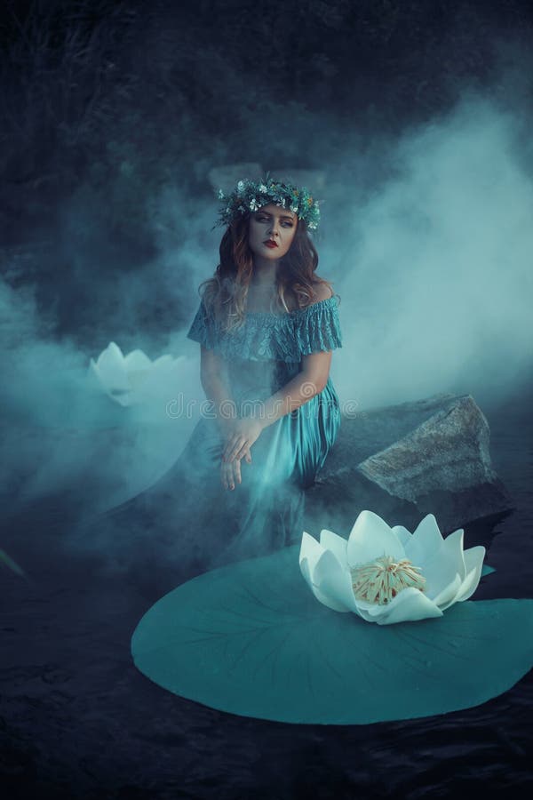 Big beautiful woman in the fog.River witch, sitting on a rock in lake among Lily casts a spell on the water. Green long dress, a wreath of herbs, a fabulous image.Fashionable toning. Creative color. Big beautiful woman in the fog.River witch, sitting on a rock in lake among Lily casts a spell on the water. Green long dress, a wreath of herbs, a fabulous image.Fashionable toning. Creative color.