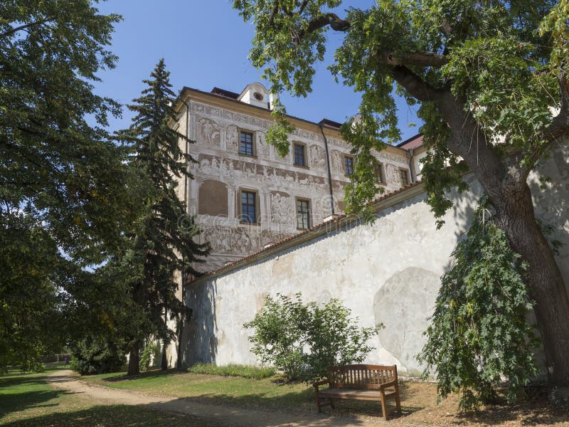 Renaissance style castle with Sgraffito decorated facade, park, footpath, green trees garden and wooden bench, sunny summer day