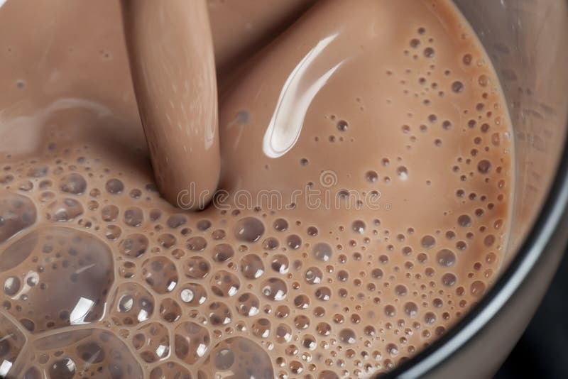 A close up of a delicious chocolate milk is being poured into a glass waiting to be drank. A close up of a delicious chocolate milk is being poured into a glass waiting to be drank.