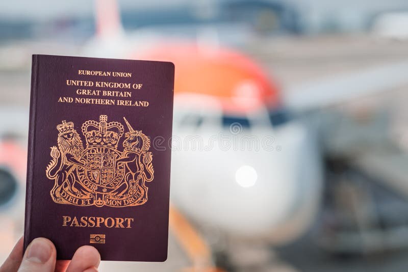 Czerwień Brytyjski paszport podtrzymujący przeciw tłu rodzajowy samolot na jaskrawym słonecznym dniu obraz stock Czerwień Brytyjski paszport podtrzymujący przeciw tłu rodzajowy samolot na jaskrawym słonecznym dniu obraz stock