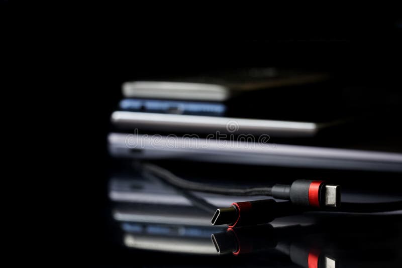 Red and black usb type-c connectors next to many modern gadgets: laptop, tablet and smartphones. Black mirror background. Connect and charge gadgets. Copy space. Selective focus. Macro. Red and black usb type-c connectors next to many modern gadgets: laptop, tablet and smartphones. Black mirror background. Connect and charge gadgets. Copy space. Selective focus. Macro