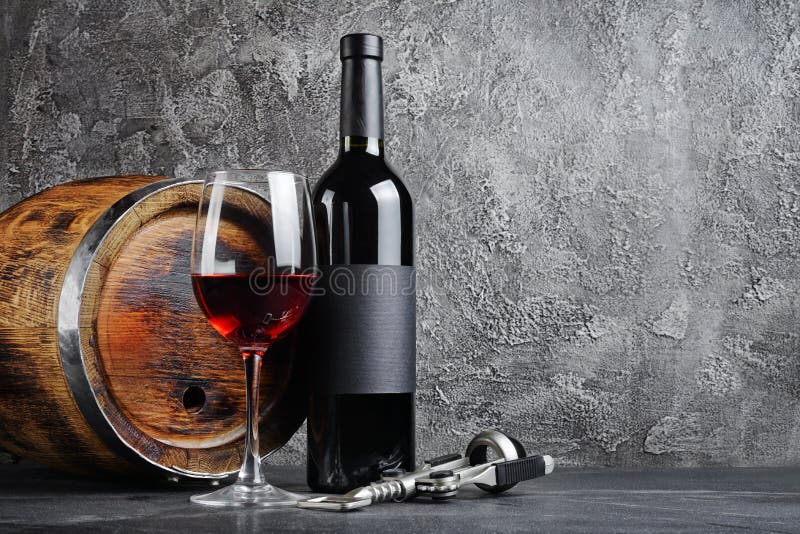 Red wine bottle with glass for tasting and wooden barrel in dark cellar on gray concrete background. Red wine bottle with glass for tasting and wooden barrel in dark cellar on gray concrete background