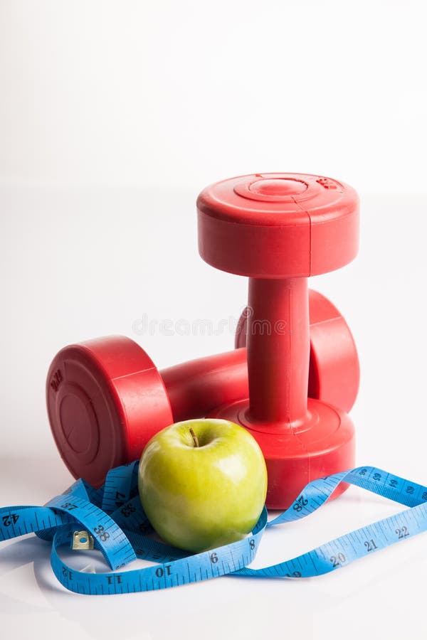 Czerwony dumbbells ciężar z pomiarowym taśmy i zieleni jabłkiem zdjęcie stock Czerwony dumbbells ciężar z pomiarowym taśmy i zieleni jabłkiem zdjęcie stock