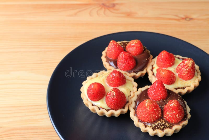 Cztery kawałka mini czekoladowi tarts nakrywający z świeżymi truskawkami i jadalnym złoto proszkiem słuzyć na czarnym talerzu zdjęcia royalty free Cztery kawałka mini czekoladowi tarts nakrywający z świeżymi truskawkami i jadalnym złoto proszkiem słuzyć na czarnym talerzu zdjęcia royalty free