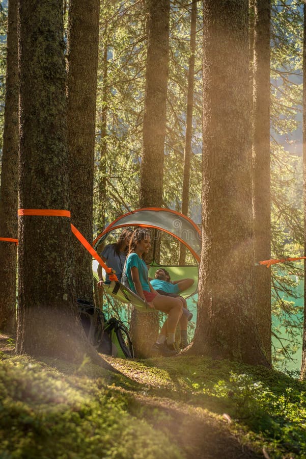 Cztery mężczyzna i kobiety szczęśliwy wiszący namiotowy camping w lasowych drewnach podczas słonecznego dnia blisko jeziora Grupa zdjęcie stock Cztery mężczyzna i kobiety szczęśliwy wiszący namiotowy camping w lasowych drewnach podczas słonecznego dnia blisko jeziora Grupa zdjęcie stock