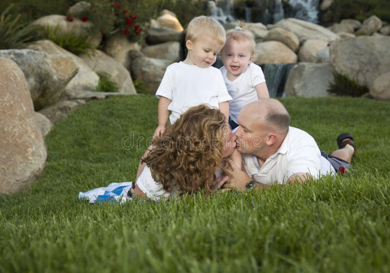 Affectionate Couple Kiss as Adorable Twins Watch in the Park. Affectionate Couple Kiss as Adorable Twins Watch in the Park.