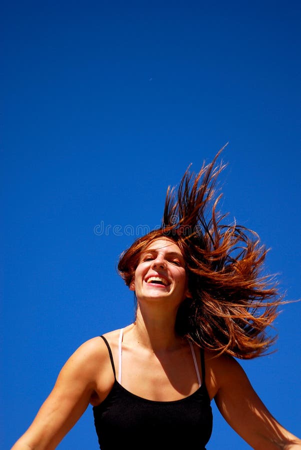 Outdoor portrait of an attractive caucasian white teenage girl with wild brunette hair and happy smiling facial expression feeling free in front of blue sky background. Outdoor portrait of an attractive caucasian white teenage girl with wild brunette hair and happy smiling facial expression feeling free in front of blue sky background