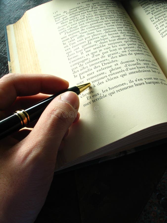 Picture of a hand holding a pen on an open book. Picture of a hand holding a pen on an open book.