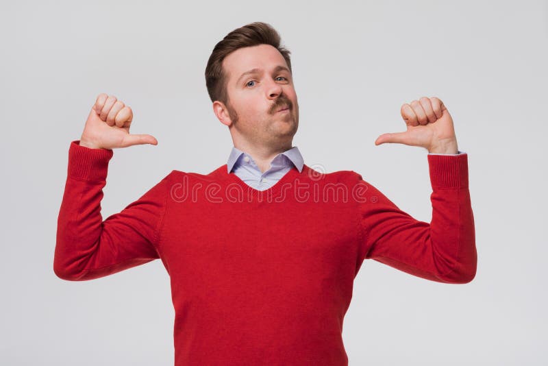 Young handsome funny man in red sweater and mustache feeling proud, arrogant and confident, looking satisfied and successful, pointing to self against flat wall. Young handsome funny man in red sweater and mustache feeling proud, arrogant and confident, looking satisfied and successful, pointing to self against flat wall