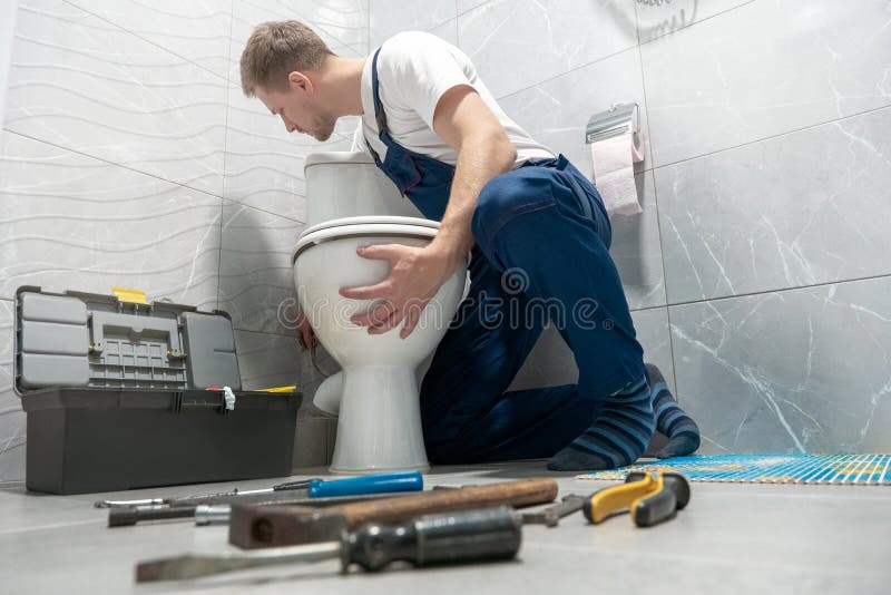 Człowiek hydraulik w mundurze instalowanie miski toaletowej przy użyciu zestawu narzędzi profesjonalna usługa naprawy