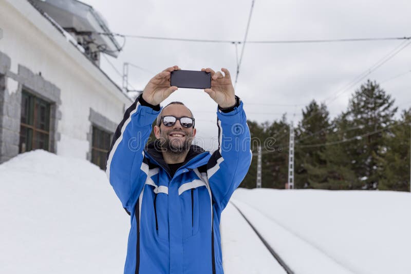 CzÅ‚owiek-wÄ™drowiec noszÄ…cy okulary przeciwsÅ‚oneczne stojÄ…cy na tle pokrytych Å›niegiem gór, zabierajÄ…cy selfie z telefonem zdjęcie stock CzÅ‚owiek-wÄ™drowiec noszÄ…cy okulary przeciwsÅ‚oneczne stojÄ…cy na tle pokrytych Å›niegiem gór, zabierajÄ…cy selfie z telefonem zdjęcie stock