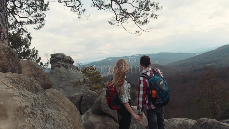 Cámara que se mueve hacia los adolescentes jovenes en amor, llevando a cabo sus manos y situación en el top de la alta montaña Él