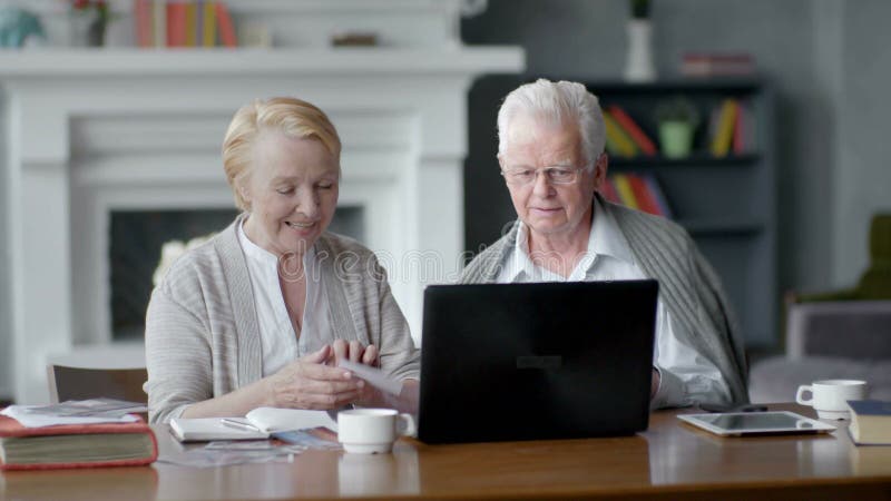 Cámara web, par mayor que se divierte en la comunicación con la familia en Internet en sala de estar cómoda