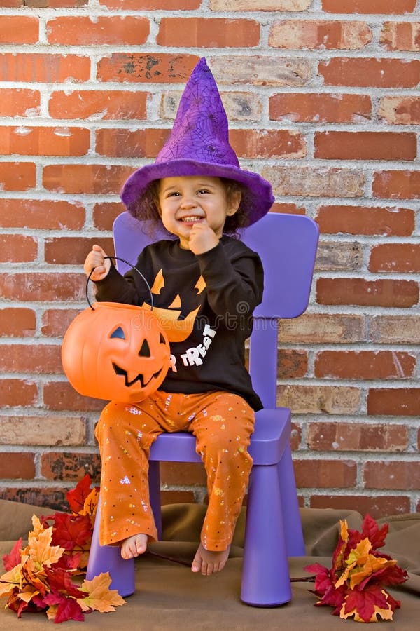 Toddler wearing halloween outfit and getting candy from her jack-o-lantern. Toddler wearing halloween outfit and getting candy from her jack-o-lantern