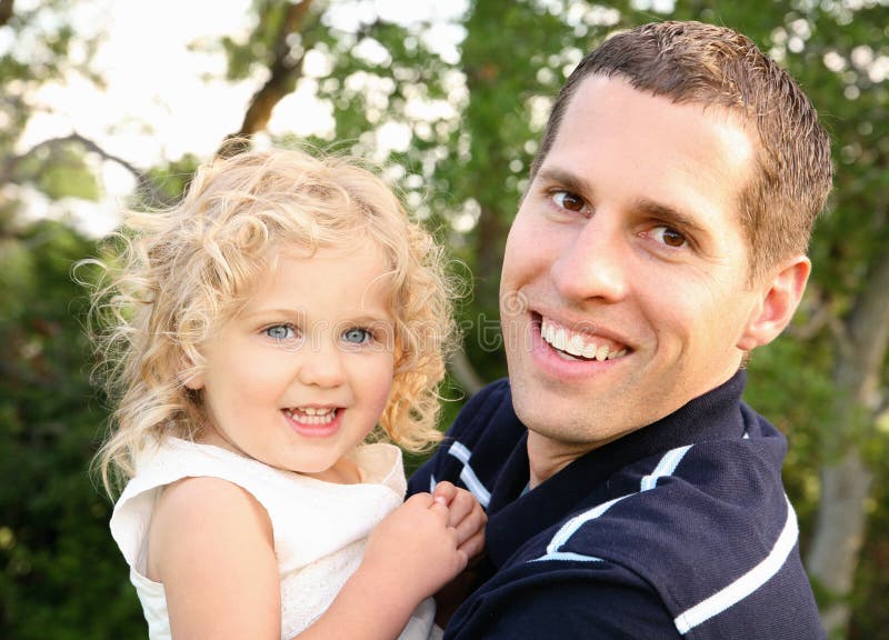 Dad and Daughter. Young Caucasian father holding his two year old daughter outdoors in Spring and smiling Dad and Daughter. Young Caucasian father holding his two year old daughter outdoors in Spring and smiling