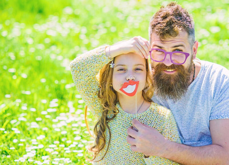 Dad and daughter sits on grass at grassplot, green background. Fatherhood concept. Family spend leisure outdoors. Child