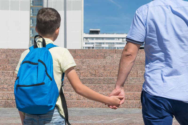 Dad is leading a boy with a backpack to school