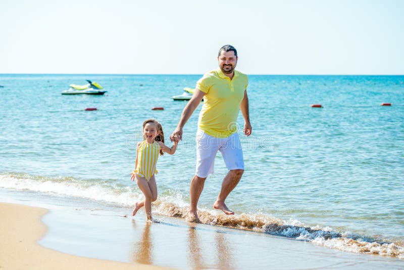 Dad and little girl play, run on the beach and fool around on the sea coast. Family vacation at sea with a child stock image Dad and little girl play, run on the beach and fool around on the sea coast. Family vacation at sea with a child stock image