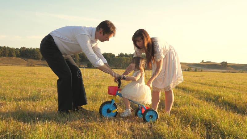 Dad and Mom teach daughter to ride a bike. Mother and father play with small child on lawn. kid learns to ride bicycle royalty free stock image Dad and Mom teach daughter to ride a bike. Mother and father play with small child on lawn. kid learns to ride bicycle royalty free stock image