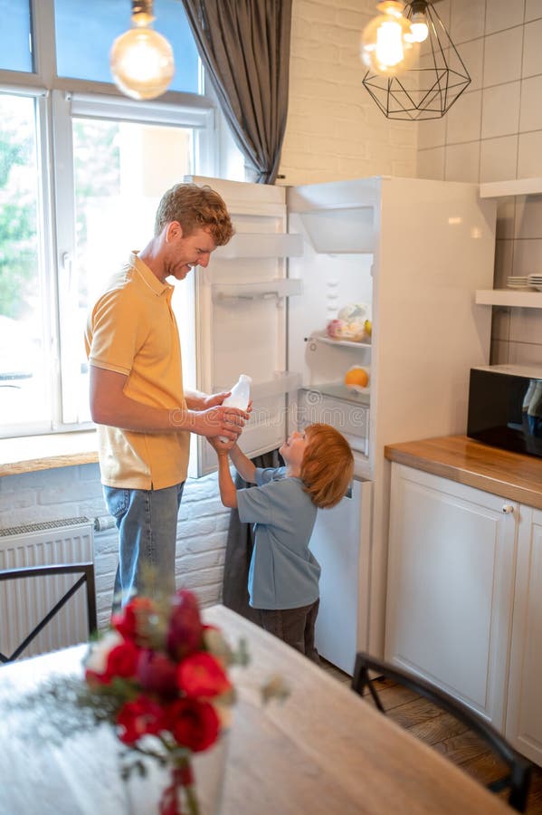 Ginger man with a bottle of milk in hands getting ready the breakfast for his son stock image