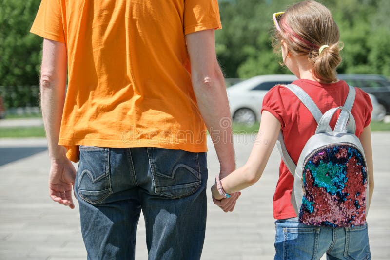 Dad walks with his daughter holding hands. Outdoor, sunny summer day, back view stock photo Dad walks with his daughter holding hands. Outdoor, sunny summer day, back view stock photo