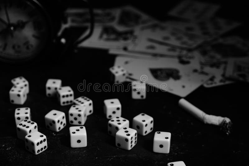 Dice,cigarettes, cards, and an abandoned alarm clock on a table in an underground casino.In black and white. Dice,cigarettes, cards, and an abandoned alarm clock on a table in an underground casino.In black and white.