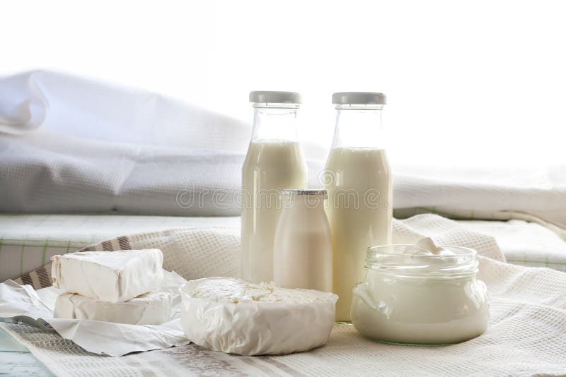 Dairy products. Milk in glass bottle, yogurt, sour milk cheese, sour cream in glass jar, camembert, brie on light wooden table royalty free stock photo