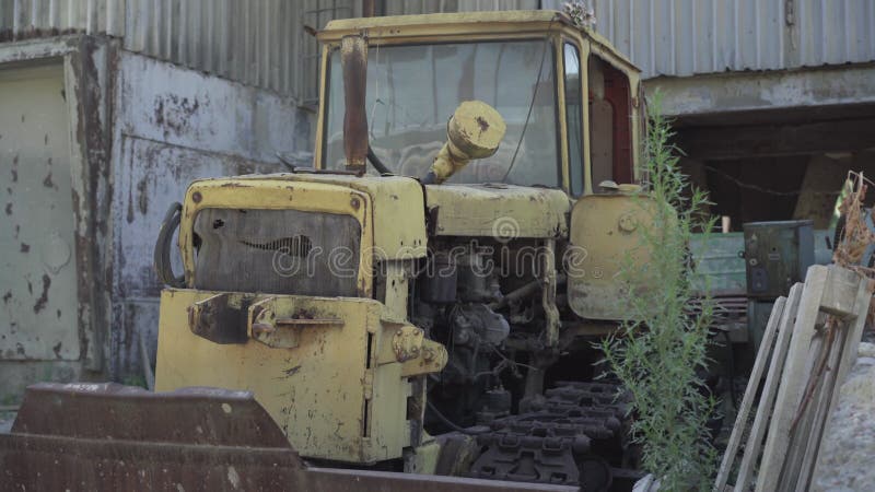 Damaged rusty tractor standing on abandoned ruins of factory. Neglected ruined machinery outdoors. Old industrial