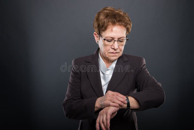 Dame supérieure d'affaires vérifiant sa montre-bracelet photographie stock libre de droits Dame supérieure d'affaires vérifiant sa montre-bracelet photographie stock libre de droits