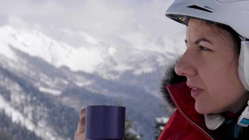 Dameskachel tegen beschermende helm drinkt warme thee koffie in skioord