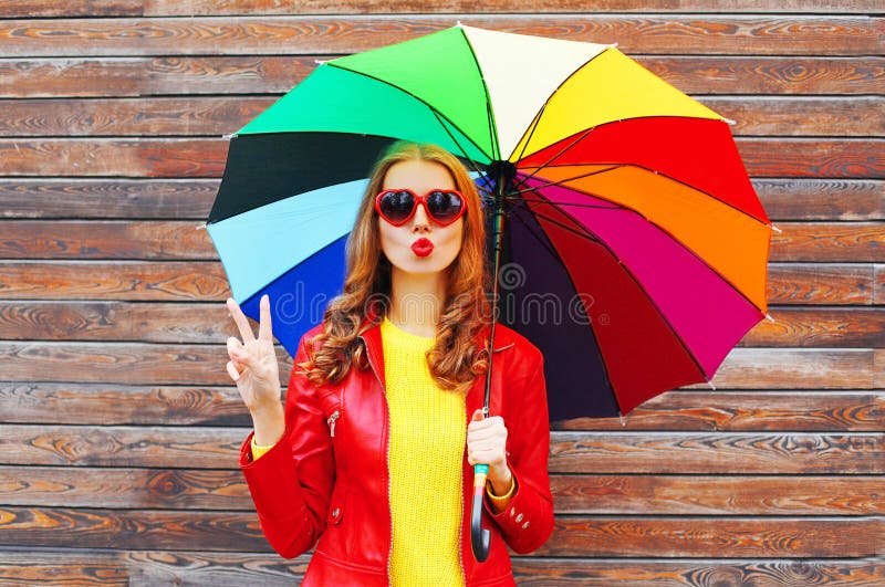 Dana den nätta kvinnan med det färgrika paraplyet i höstdag över träbakgrund som bär det röda läderomslaget