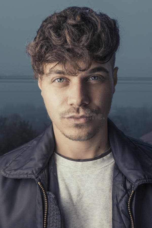 Dana ståendefotoet av den unga och stiliga mannen med det lockiga frisyr- och läderomslaget Manlig modellstående med den nätta bl fotografering för bildbyråer Dana ståendefotoet av den unga och stiliga mannen med det lockiga frisyr- och läderomslaget Manlig modellstående med den nätta bl fotografering för bildbyråer