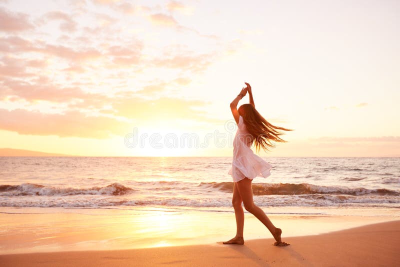 Dancing spensierato felice della donna sulla spiaggia al tramonto