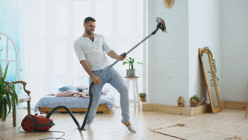 Young man having fun cleaning house with vacuum cleaner dancing like guitarist