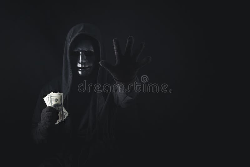 Dangerous anonymous hacker man in hooded showing stop gesture and holding banknote, break security data and hack password with personal Bank account. Internet crime cyber attack security concept. Dangerous anonymous hacker man in hooded showing stop gesture and holding banknote, break security data and hack password with personal Bank account. Internet crime cyber attack security concept
