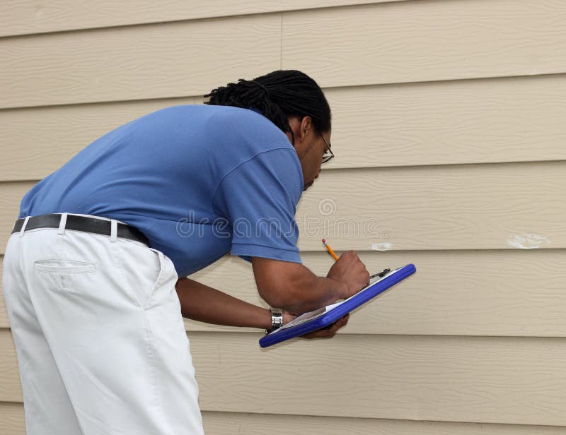 An insurance adjuster marks hail damage dings with white chalk and records his findings for a homeowner storm damage claim. An insurance adjuster marks hail damage dings with white chalk and records his findings for a homeowner storm damage claim.