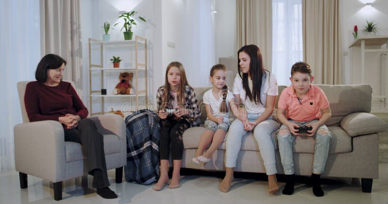 Dans a il salon une mère avec trois enfants et mamie passent un bon temps ensemble tandis que des enfants jouant sur un jeu vidéo