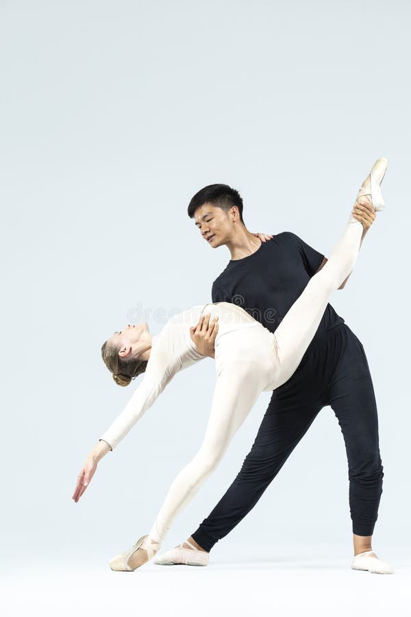 Dansa ett par unga män och en kaukasisk kvinna som utför balettdansare över grå i studio under föreställningar som klassisk dans. Dansa ett par unga män och en kaukasisk kvinna som fungerar som balettdansare över grå i studio under föreställningar som klassisk dans med koreografiska element vertikal sammansättning