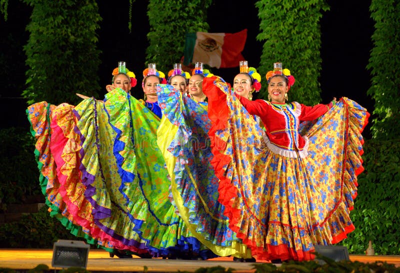 Mexican female folkloric ballerinas in colorful costumes dancing with a glass placed on the heads. Mexican female folkloric ballerinas in colorful costumes dancing with a glass placed on the heads