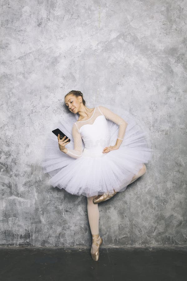 Danseuse classique de jeune ballerine en utilisant le téléphone portable contre le mur rustique images stock