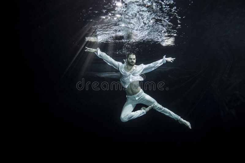 A young male ballet dancer is dancing underwater. A young male ballet dancer is dancing underwater