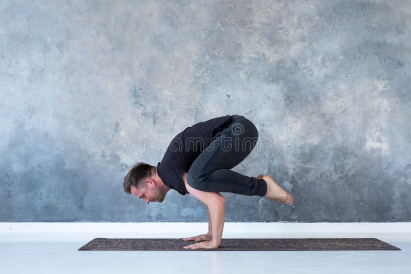Dar certo desportivo do homem novo, fazendo o asana da ioga do pino, a pose do corvo ou o Bakasana imagem de stock royalty free Dar certo desportivo do homem novo, fazendo o asana da ioga do pino, a pose do corvo ou o Bakasana imagem de stock royalty free