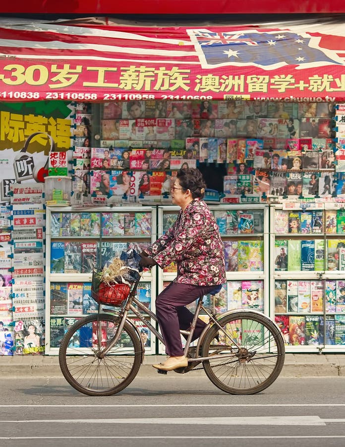 Dar um ciclo pessoas idosas fêmeas chinesas passa uma livraria exterior, Tianjin, China imagem de stock Dar um ciclo pessoas idosas fêmeas chinesas passa uma livraria exterior, Tianjin, China imagem de stock